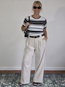 Woman over 40 in a black-and-white striped top and cream wide-leg trousers with a black bag
