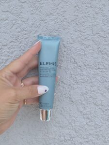 Hand holding an ELEMIS sunscreen tube outdoors
