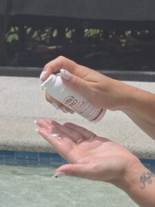 Applying a sunscreen mist onto the back of a hand by the pool