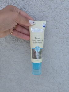 Hand holding a Bliss tinted mineral sunscreen tube