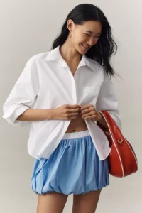 Model in an oversized white button-down shirt with a red bag