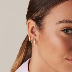 Close-up of an ear wearing small gold huggie hoop earrings