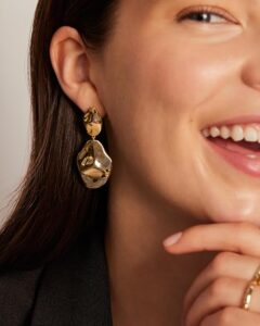 Woman over 40 wearing a sculptural gold teardrop statement earring