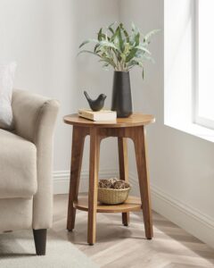 Round wooden side table with a potted plant and stacked books beside a cream armchair
