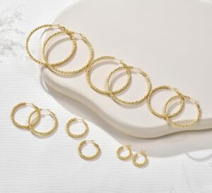 Twisted textured gold hoop earrings in several sizes on a cream surface