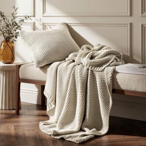 Cream chunky-knit throw draped over a bench with a matching textured knit pillow
