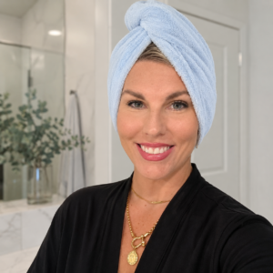 Smiling woman over 40 with wet hair wrapped in a light blue microfiber towel turban, wearing a black robe