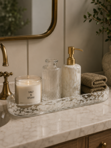 A styled bathroom counter with a marble tray, candle, glass soap dispensers and folded towels for an uncluttered look