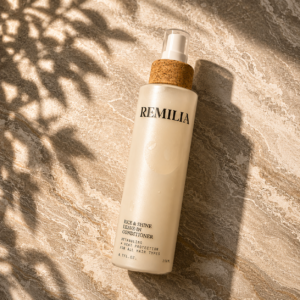Remilia leave-in conditioner spray bottle on a beige marble surface with soft leaf shadows