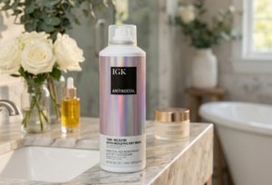 IGK leave-in hair product bottle on a marble counter with white roses and hair oil