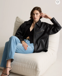 Woman over 40 in a black leather jacket and blue jeans relaxing on a cream chair — elegant leather jacket styling